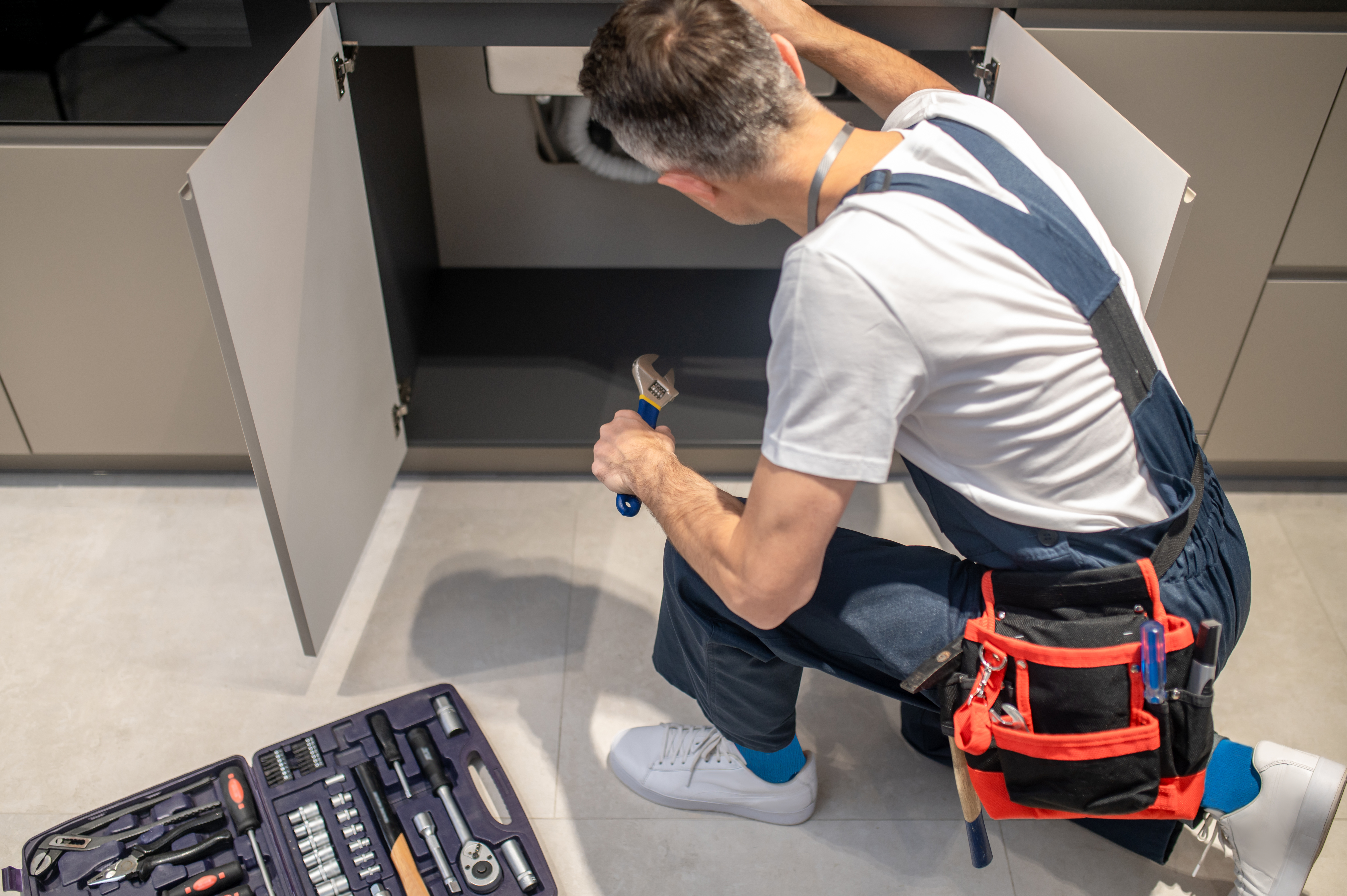 Plombier répare sous évier avec outils.